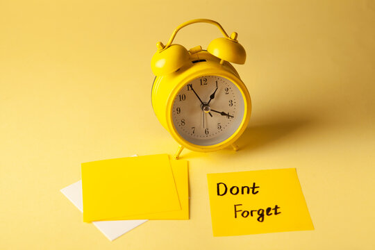 Yellow alarm clock and yellow sticky notes with text Don't forget on yellow background
