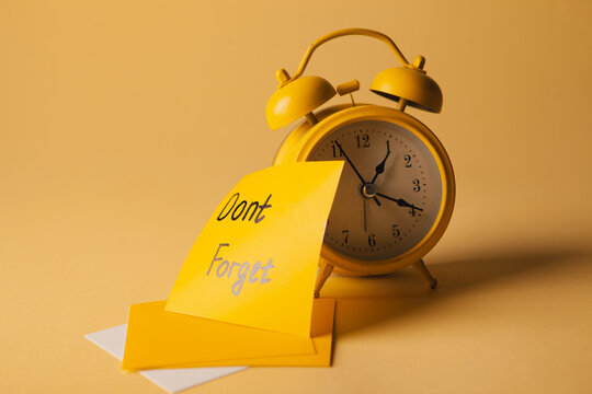 Yellow alarm clock and yellow sticky notes with text Don't forget on yellow background