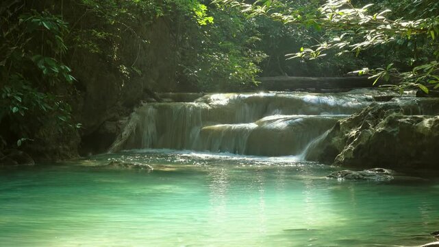 View of the turquoise tiered pools of Erawan Falls surrounded by dense tropical forest in Tha Kradan, Kanchanaburi, Thailand.