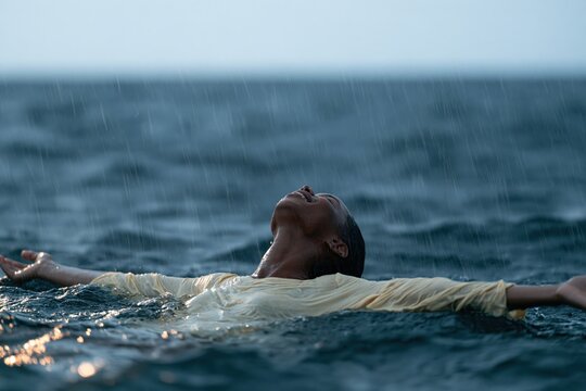 Person floating in rain soaked ocean with arms outstretched for moody seascape wallpaper and wellness background focused on calm and reflection