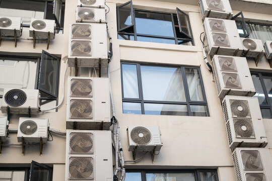 many air conditioner units hang on residential building facade. heavy load of air conditioner equipment cools apartment in hot summer. urban air conditioner shows city life reality