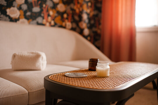 Glass bottle of scented candle on rattan table over living room interior close up. Cozy atmosphere.