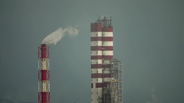 View of industrial chimneys with red and white stripes emitting smoke against a grey sky in Russia.