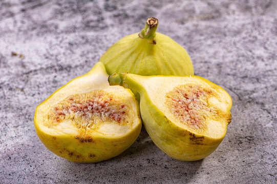 Fresh yellow figs cut in half showing pinkish seeds and juicy interior on textured gray surface