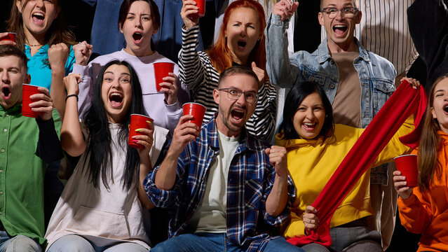 Diverse sports crowd waves colorful scarves while shouting in packed stadium with intense excitement. Sports fandom, crowd energy and team support concept.