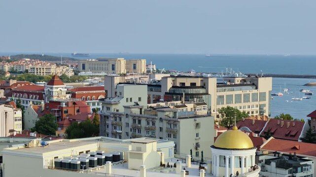 A high-angle view of a coastal city with mixed architecture, a pier extending into the sea, and a small island in the harbor under clear sky.