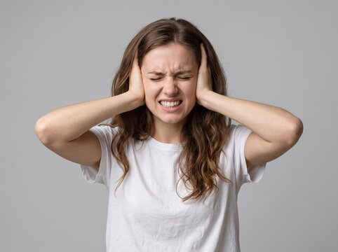 Young woman suffering from severe migraine headache, covering ears with hands, experiencing stress and chronic pain