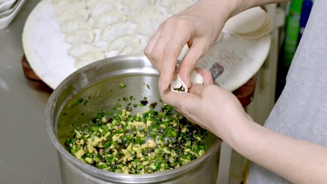 A person wraps dumplings, placing vegetable and egg filling onto a dumpling wrapper over a metal bowl.