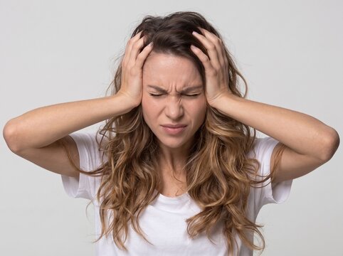 Portrait of a stressed young woman clutching her head in pain from a severe migraine