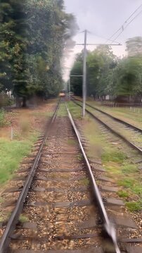 Commute in the public transport on the rainy day. A tram with headlights on is approaching, but keeps the safe distance