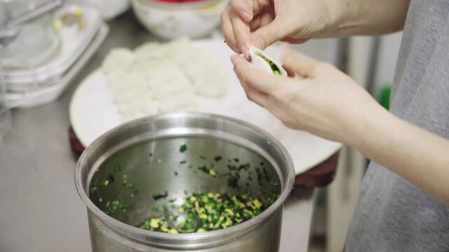 A person adds vegetable filling to dumpling wrappers during food preparation in a kitchen.