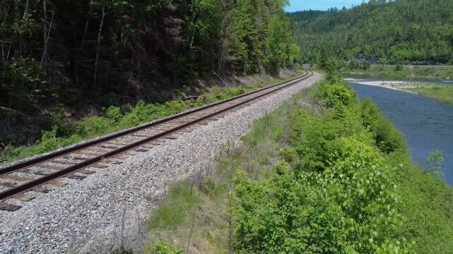 Aerial video captures railroad tracks bordering a dense forest and the Matapedia River, where clean gravel and discarded ties provide evidence of ongoing infrastructure improvements.
