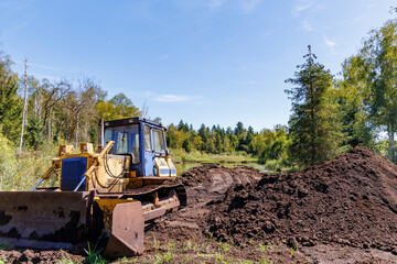 Heavy crawler bulldozer and piles of dark peat soil at wetland restoration and moorland clearing site under clear blue sky, ecological conservation and earthmoving concept © JaRu Creative Studio