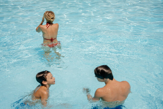 Mother watching her two sons play together during relaxed summer day in outdoor swimming pool