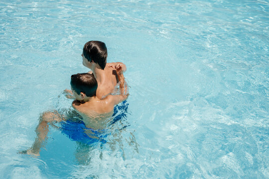 Brothers hugging and playing together in swimming pool during carefree sunny summer vacation
