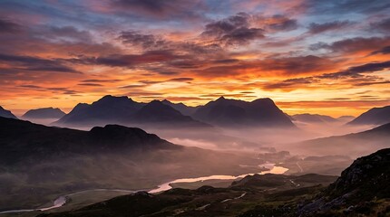 Obraz premium A vibrant sunset glows behind dark mountain silhouettes with a misty valley with clouds illuminate mountain