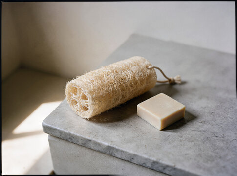 Natural loofah sponge on a light gray stone surface, fibrous plant texture, soft light from the left