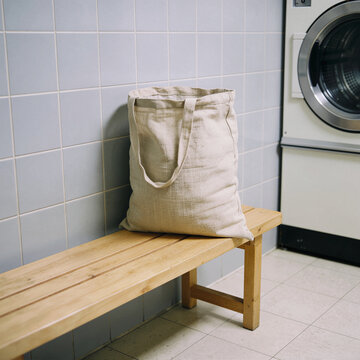 Laundry room corner with a canvas laundry bag on a light wooden stool, gray tile wall, soft daylight