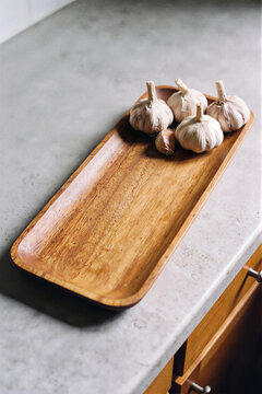 Wooden serving board on a light gray stone surface with a few garlic cloves on the edge