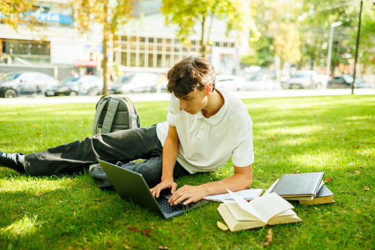Focused Young Scholar Working On A Computer On The Green Park Lawn.
