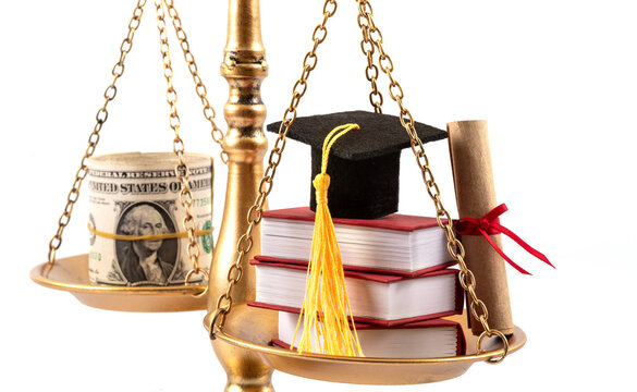 An academic cap, books, a diploma, and a stack of US 1 dollar bills on the pans of a balance scale.
