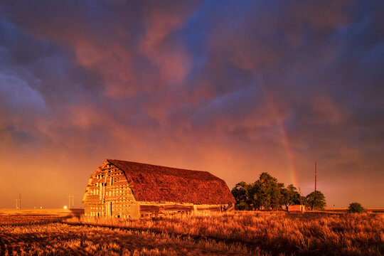 Old barn at sunset with rainbow and storm clouds