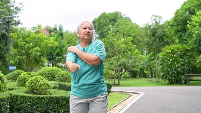 Senior Woman Stretching in the Park: A senior woman diligently stretches her shoulder in the tranquility of a park.