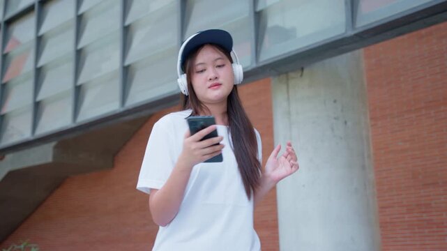 Teenager wearing headphones dancing happily outdoors, symbolizing youth lifestyle, music enjoyment, freedom, and wellness in urban environment with concrete columns, daylight, and positive atmosphere