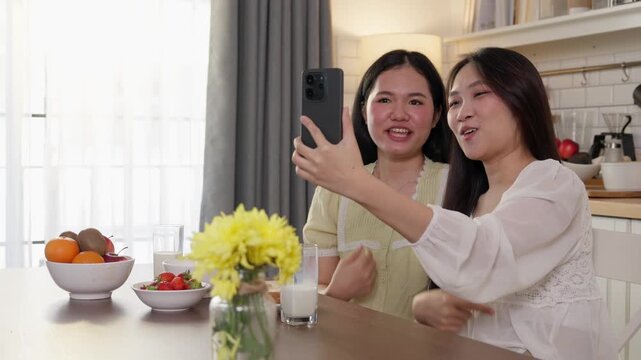 Two women use a smartphone together while taking selfies and enjoying a friendly moment at home. Suitable for social media, friendship, digital communication, female lifestyle, modern home concepts.