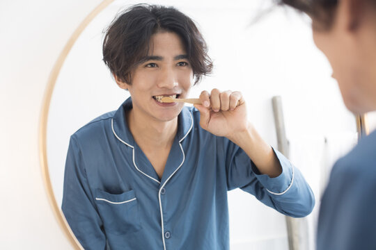 Happy young man brushing teeth in mirror during morning routine