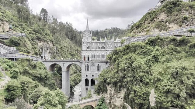 View of Las Lajas Sanctuary, a stunning Gothic-style church nestled within a deep canyon, surrounded by lush green mountains and a flowing river in Las Lajas, Narino, Colombia.