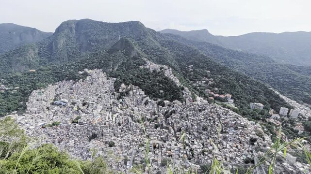 View of the dense hillside housing of Rocinha favela nestled against lush green mountains overlooking the coastal urban landscape of Rio de Janeiro, Rio de Janeiro, Brazil.