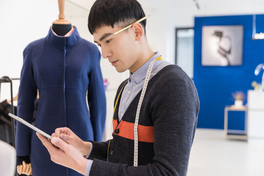 Young Asian Male Fashion Designer Using Tablet in Studio with Mannequin