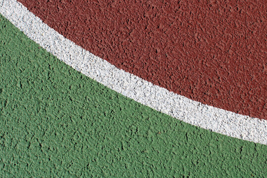 Gros plan sur les lignes de marquage blanches d'un terrain de sport ext&eacute;rieur en rev&ecirc;tement synth&eacute;tique vert et rouge bordeaux.