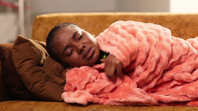 African woman feeling sick having fever and headache, sleeping on a sofa wrapped in a blanket