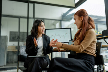 Two Asian businesswomen collaborating, discussing financial data and investment growth during a...
