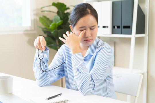Eye problem concept, fatigue asian young woman take off glasses, tired eyes irritated eye dry relief vision pain after work, eye strain, hand holding glasses, suffer bad blurry at office.
