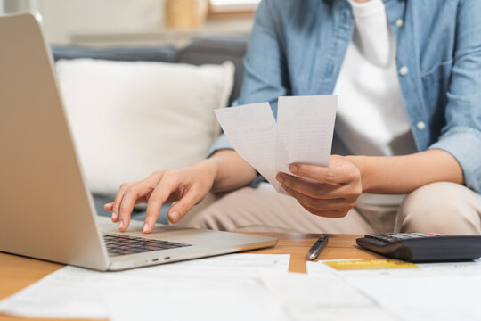 Close up of a person hand holding receipts while using laptop and calculator for home budget planning, financial management, monthly expense tracking and tax calculation