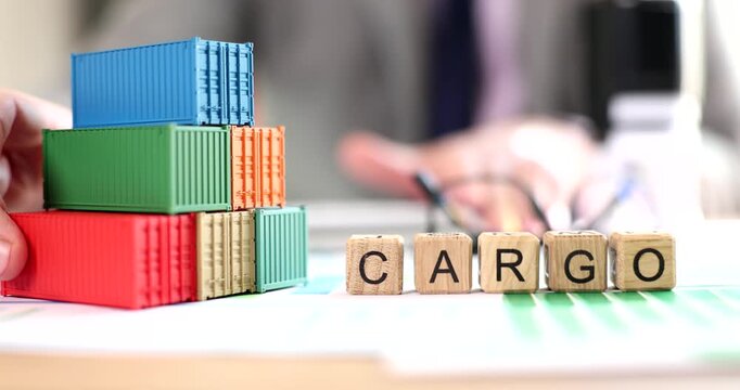 Colorful building blocks are stacked neatly, forming the word cargo. A hand reaches toward the blocks, conveying a sense of purposeful action in a professional setting.