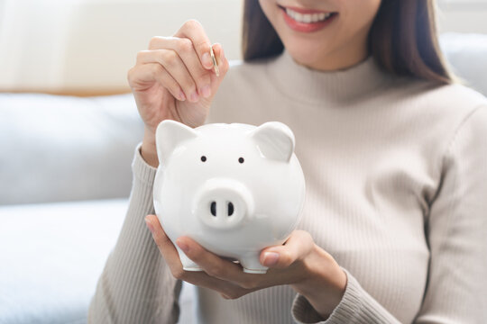 Saving money wealth concept, asian young business woman hand putting coin into piggy for saving cost, cash finance planning to spend enough money on her income for save money, payment tax, investing.