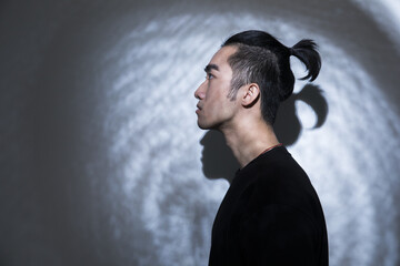 Side profile portrait of a young man with a top knot hairstyle against a shadowed wall © LamHao