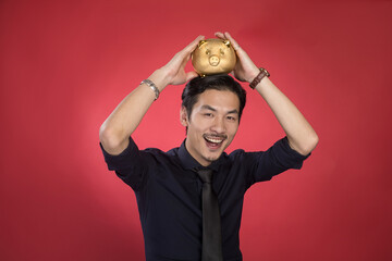 Happy Asian Businessman Holding Golden Piggy Bank on Red Background © LaDieuNgoc