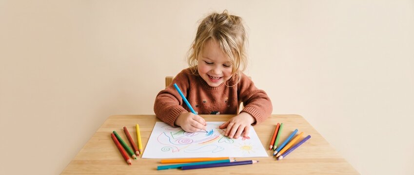 Young girl coloring with crayons at a wooden table indoors  