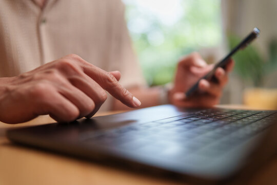 Asian Man browsing with a smartphone and laptop at home, representing online digital communication, technology and modern lifestyle.