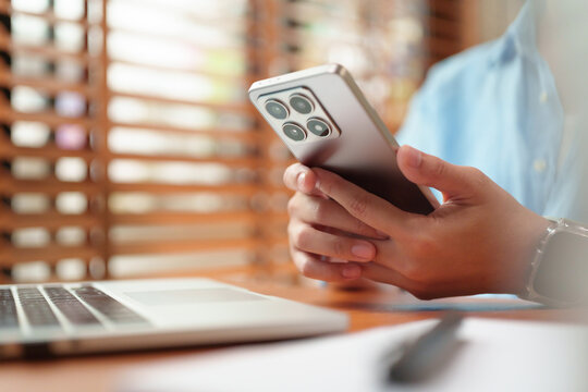 Woman using a smartphone beside a laptop at home, representing mobile apps, online browsing, digital communication, remote work, multitasking, connectivity and modern technology.