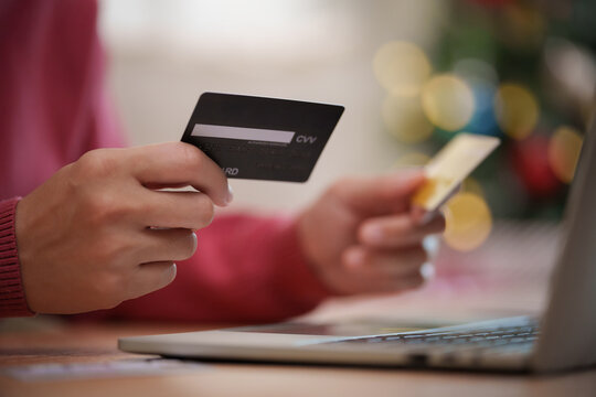 Woman holding two credit cards while shopping online on a laptop during Christmas, representing holiday spending, digital payment, e-commerce, banking, retail and seasonal sales.