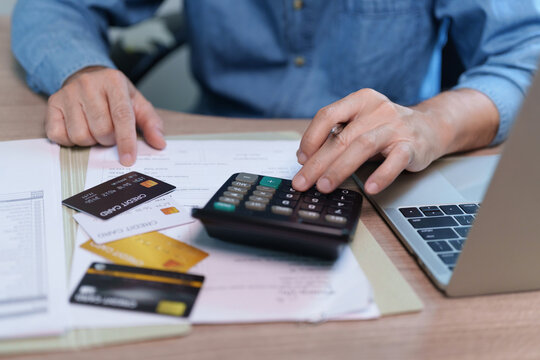 Man calculating bills and credit card payments beside a laptop at home, representing debt management, personal finance, monthly expenses, budgeting, borrowing and financial responsibility.