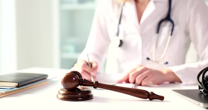 A medical professional in a white coat considers important topics while writing notes. A gavel rests nearby, symbolizing the intersection of law and healthcare in this sterile environment.