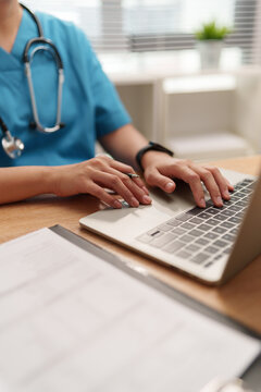Doctor working on a laptop in a clinical office with medical documents, representing digital healthcare, patient care, hospital technology.