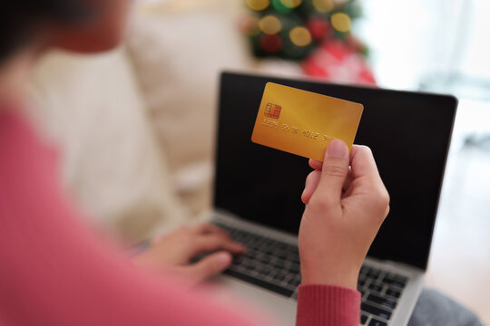 Woman holding a credit card while shopping online on a laptop at home during Christmas, representing holiday payment, e-commerce, festive retail, banking and seasonal spending.